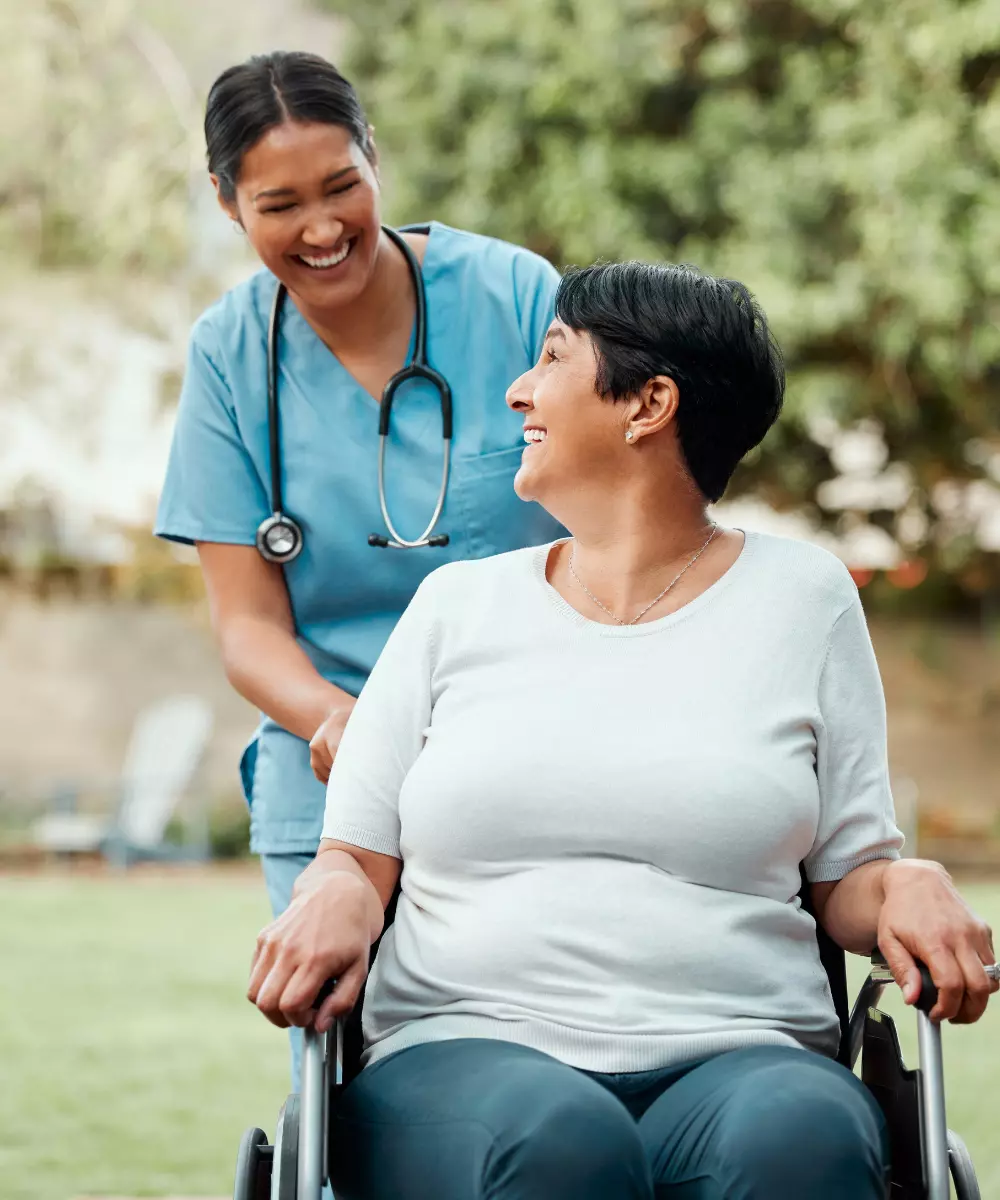 Woman in wheelchair smiling up and looking at nurse