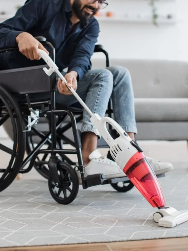 Man in wheelchair vacuuming rug at home in lounge room