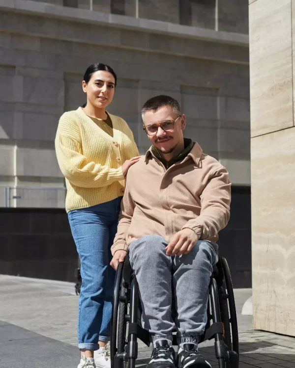 Carer with man in wheelchair both looking at camera